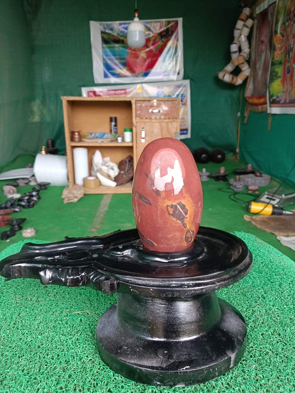 Deep red Narmadeshwar Shivling with white quartz markings on a black yoni pitha in the Bakawan workshop