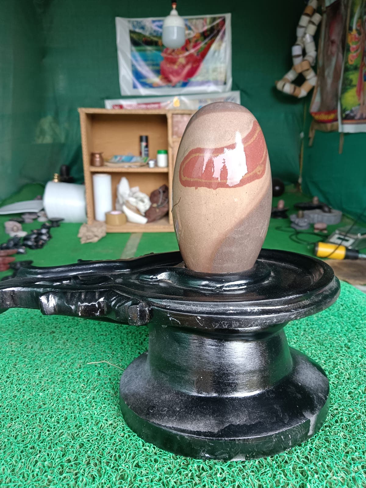 Sandy beige Narmadeshwar Shivling with a rust-coloured natural vein, seated on a black granite base