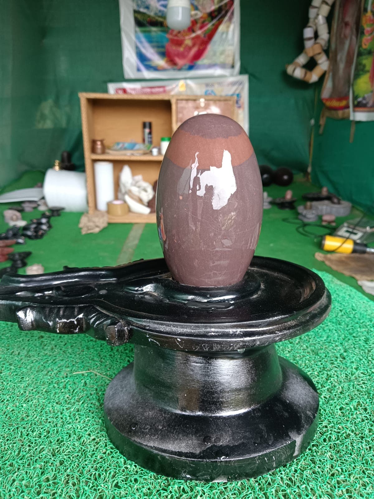 Glossy maroon Narmadeshwar Shivling after jalabhishekam, water still beading on the black stone yoni pitha