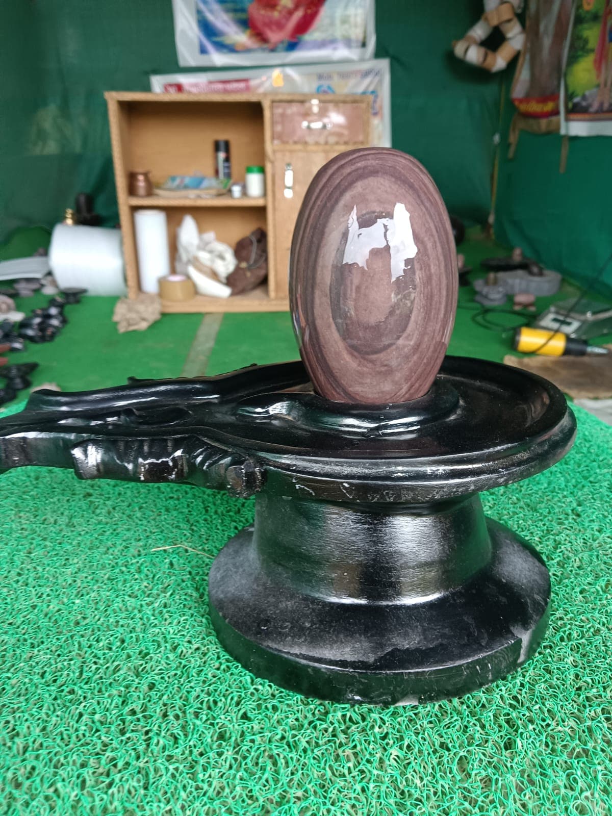 Dark brown Narmadeshwar Shivling with a white natural marking, mounted on a carved black granite jaldhara