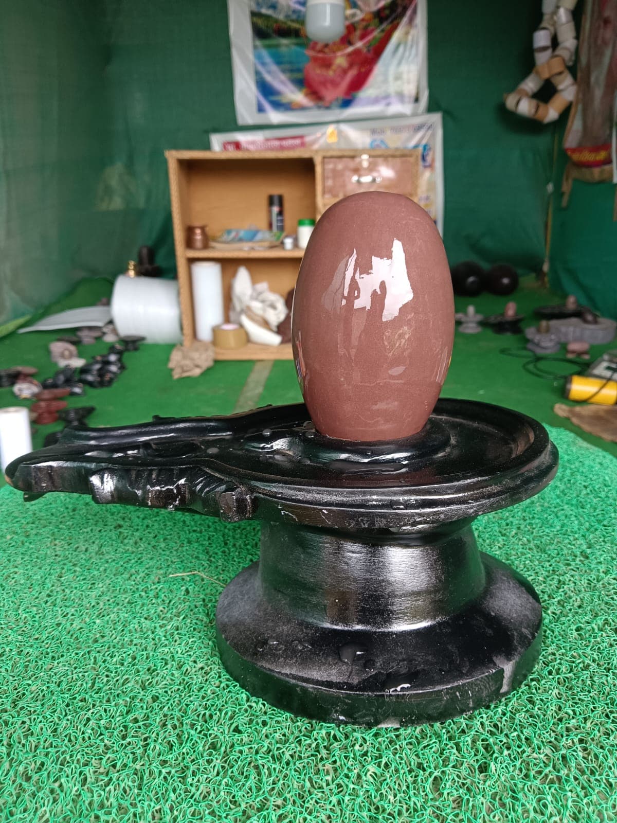 Large polished maroon Narmadeshwar Shivling with white markings on a black granite yoni pitha