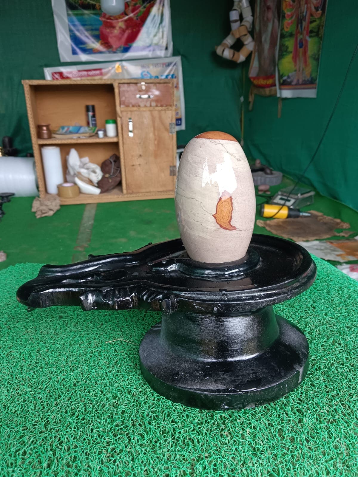 Beige Narmadeshwar Shivling with an orange base band, mounted on a black granite yoni pitha