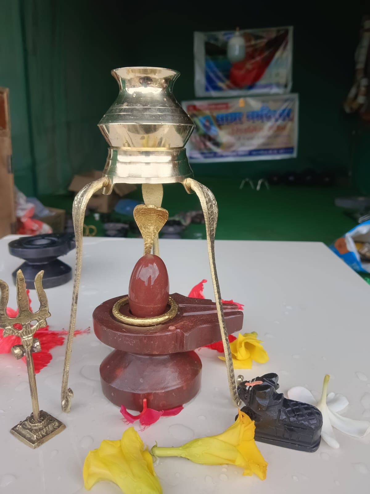 Brass abhishek patra suspended above a Narmadeshwar Shivling on a maroon marble base, with Nandi idol