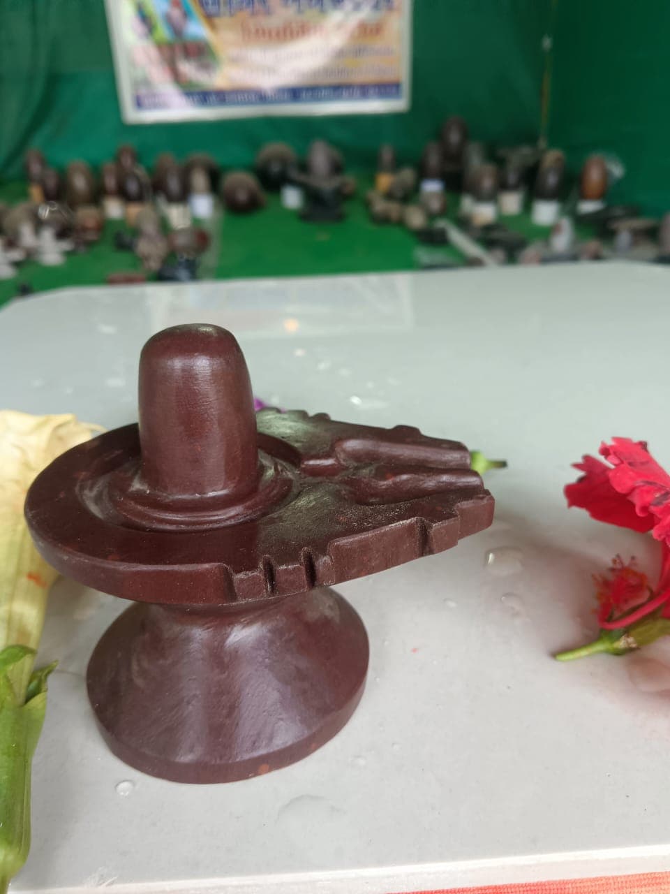 Dark maroon Narmadeshwar Shivling set into a matching maroon stone jaldhara with a drainage spout