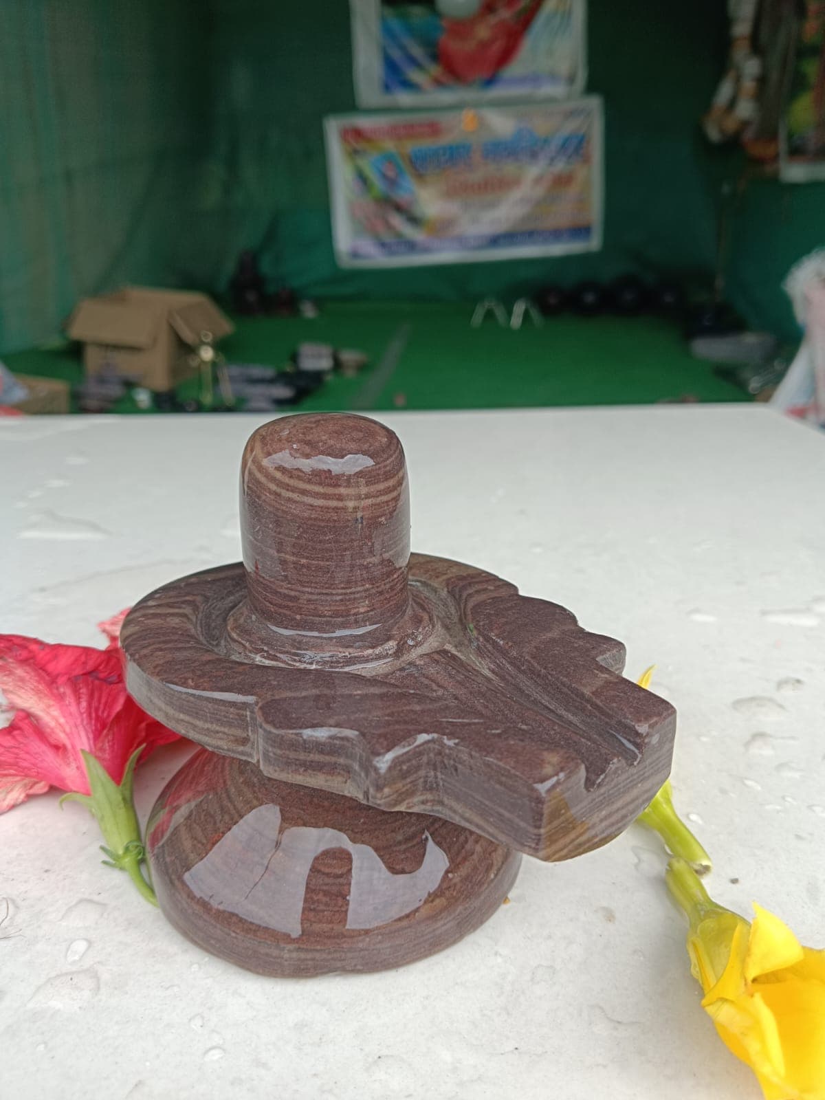 Banded brown Narmadeshwar Shivling on a maroon marble yoni pitha with red and yellow flowers
