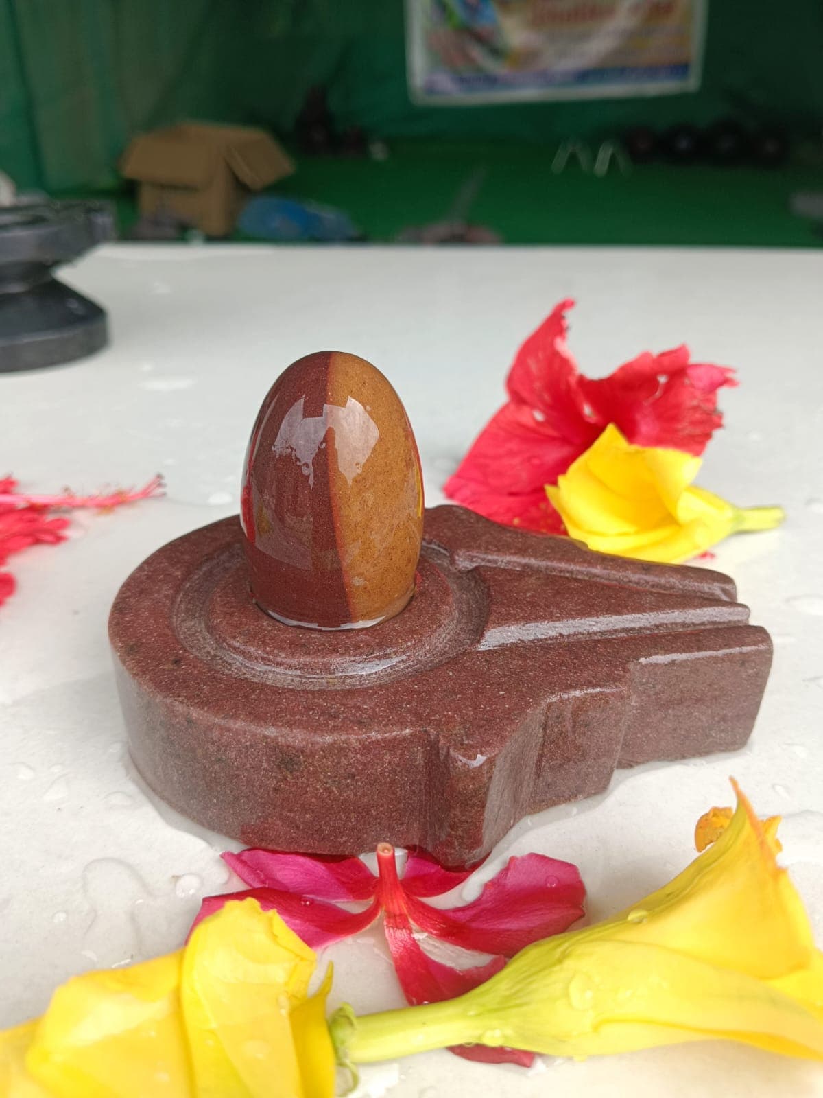 Golden-amber Narmadeshwar Shivling on a brown marble jaldhara base with yellow and red flower offerings