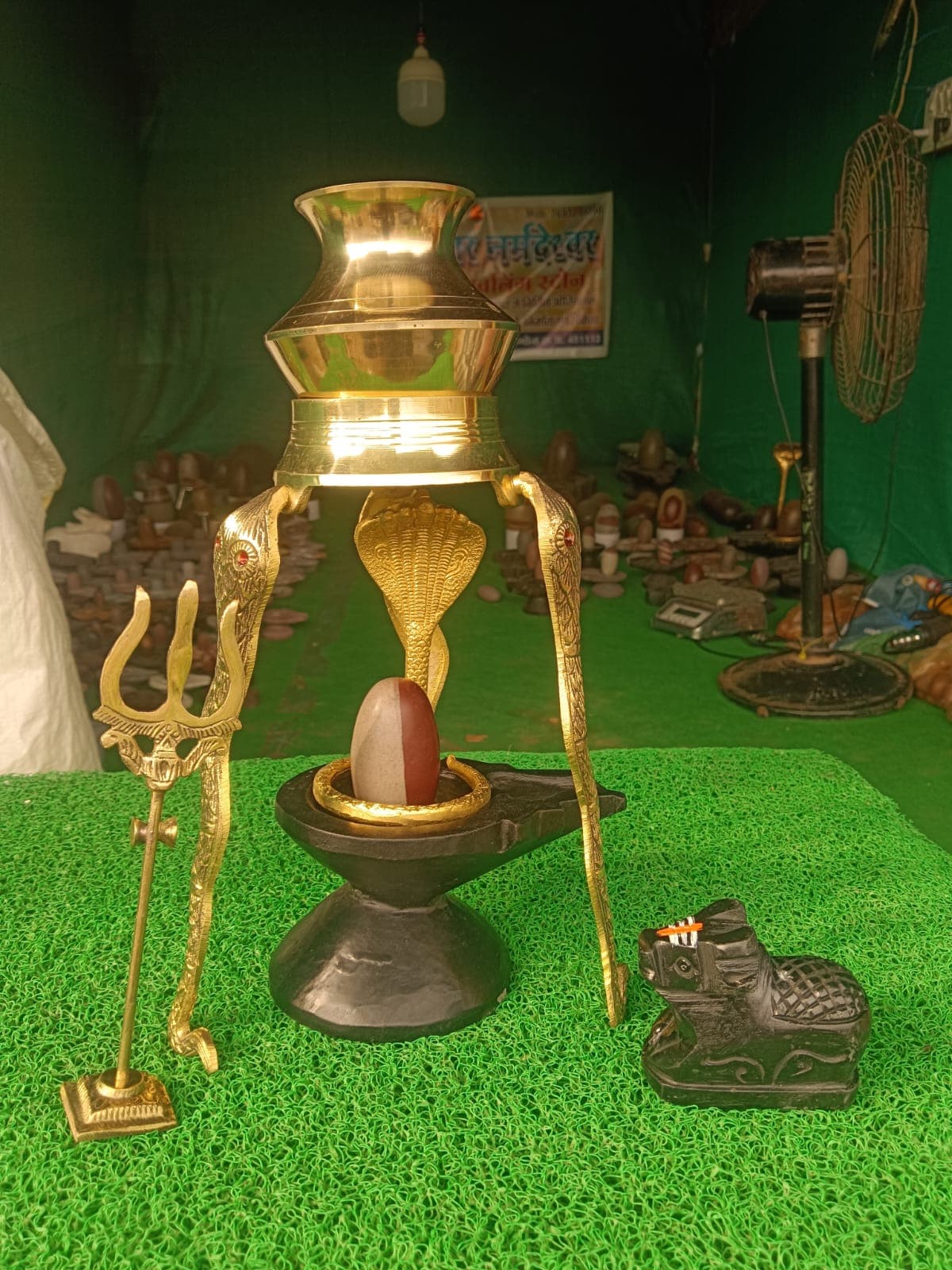 Complete Shiva puja setup: brass kalash abhishek stand over a Narmadeshwar Shivling with trishul and Nandi
