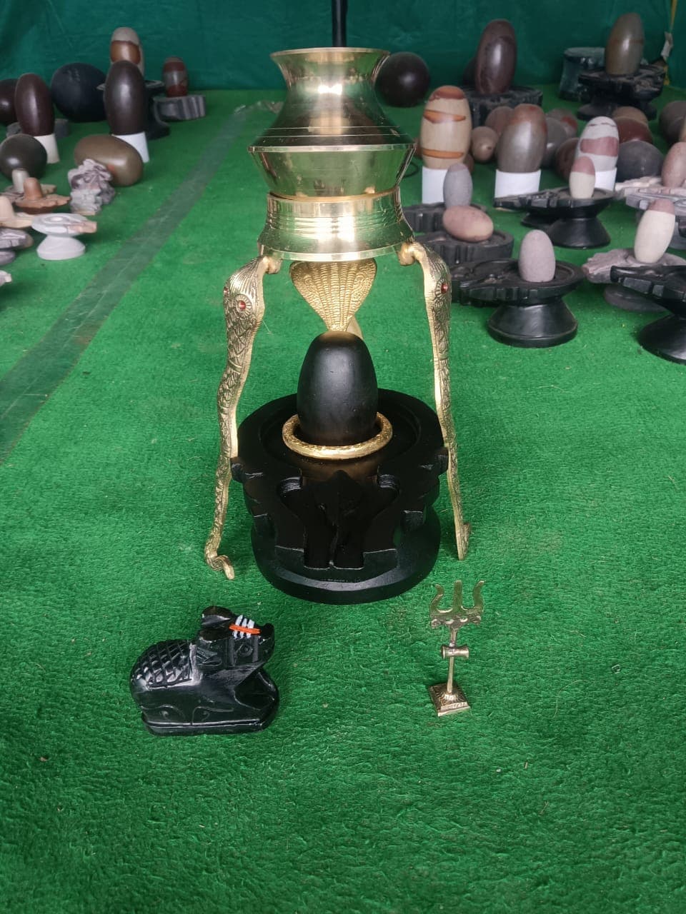Brass jalabhishekam kalash mounted above a black Shivling with trishul, damru and Nandi for Shravan puja