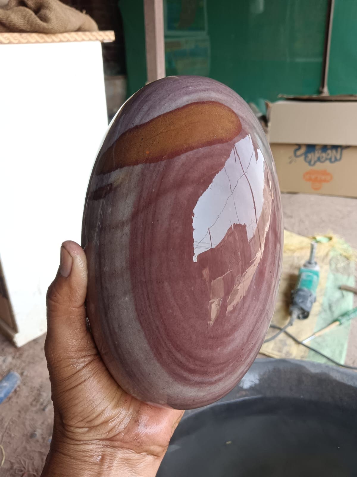 Large mauve Narmadeshwar Shivling held in hand to show its size before mounting on a yoni pitha