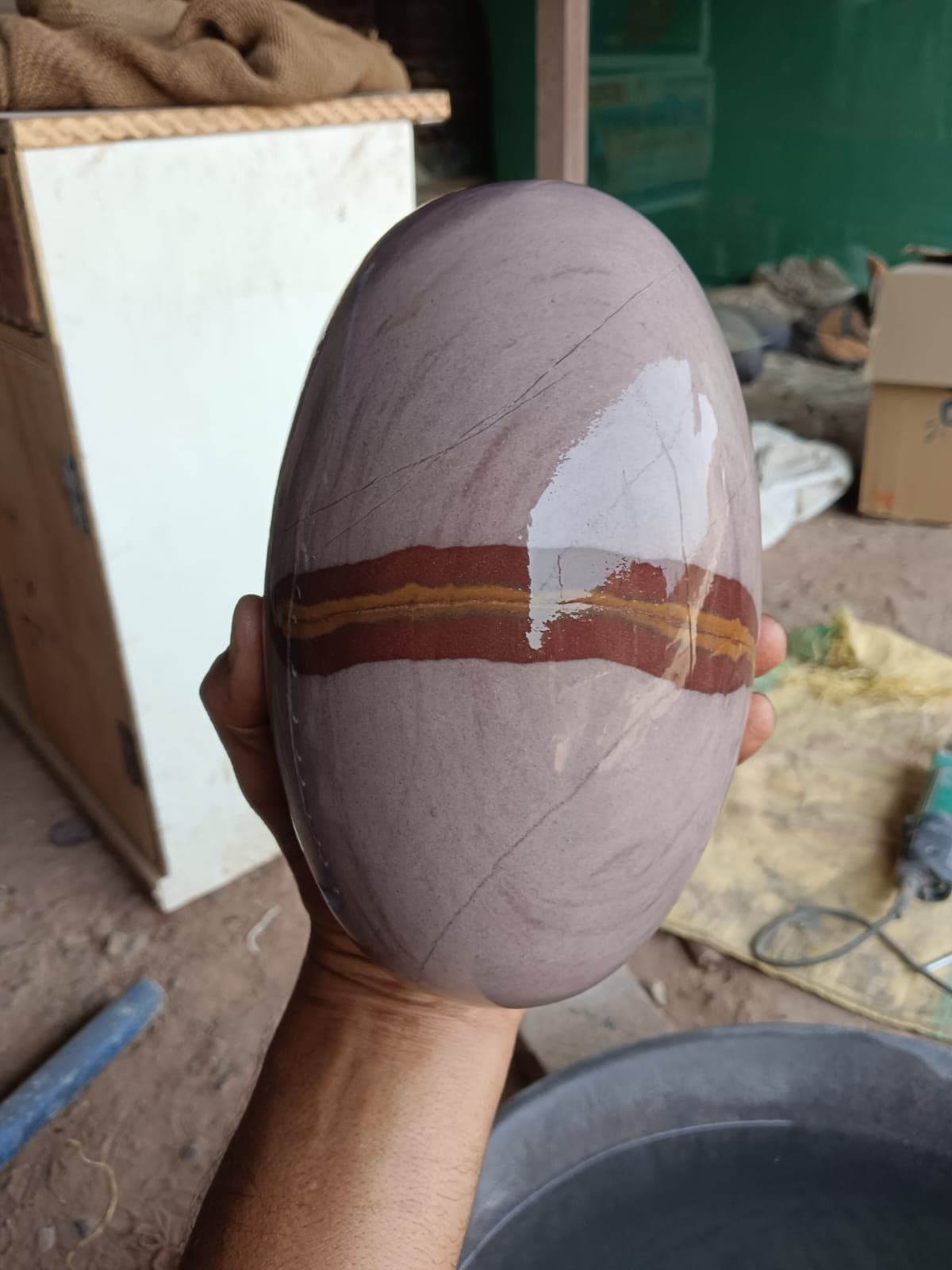Large mauve Narmadeshwar Shivling with an orange band held in hand, showing full palm-to-fingertip size
